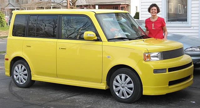 Woman standing next to a yellow Scion xB