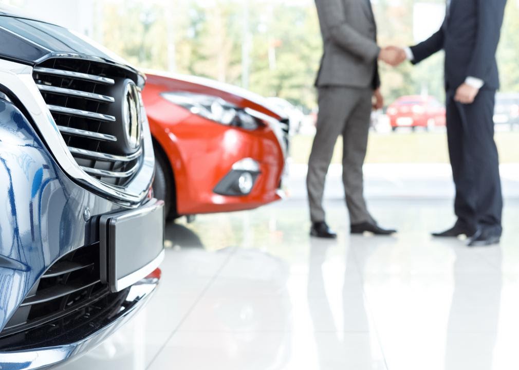 Photo of two people shaking hands in the background of a photo, with close-ups of cars in the foreground