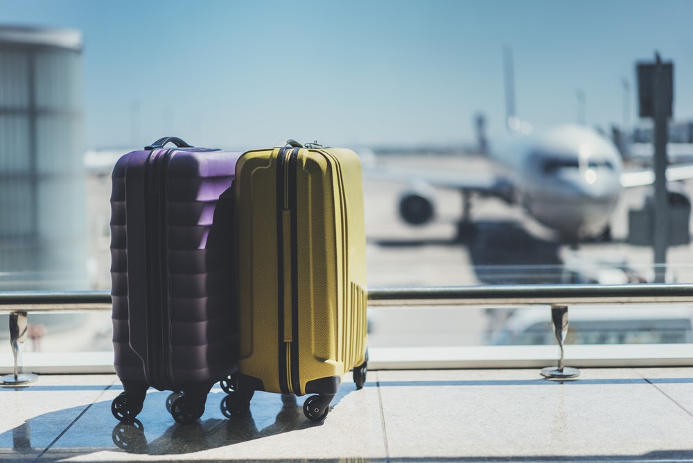 Photo of two suitcases sitting in an airport, with an out-of-focus jet in the window behind them